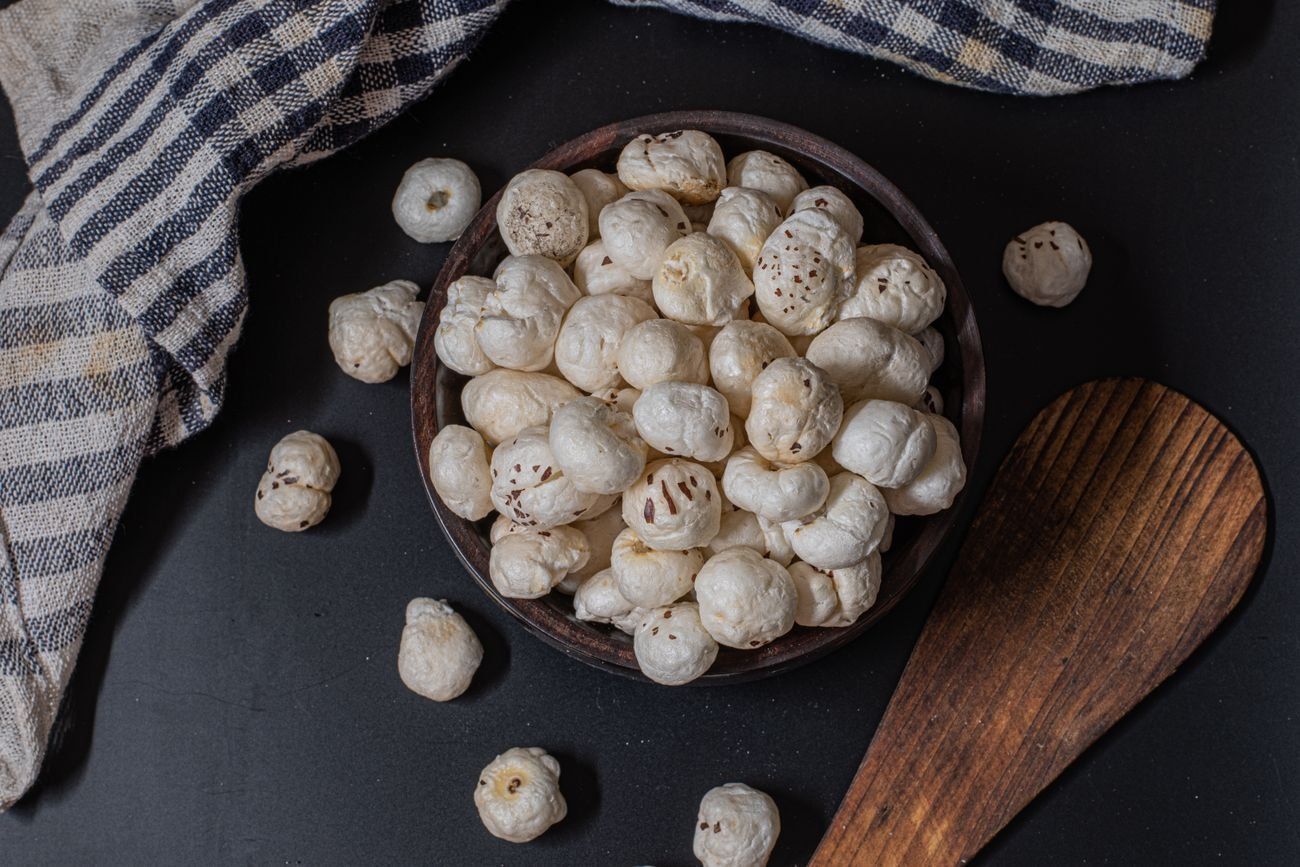 A rustic dark bowl of roasted makhana foxnuts with a wooden spoon on a moody slate surface
